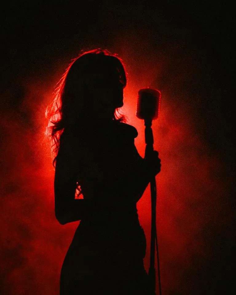 Red-backlit silhouette of a singer at a vintage microphone