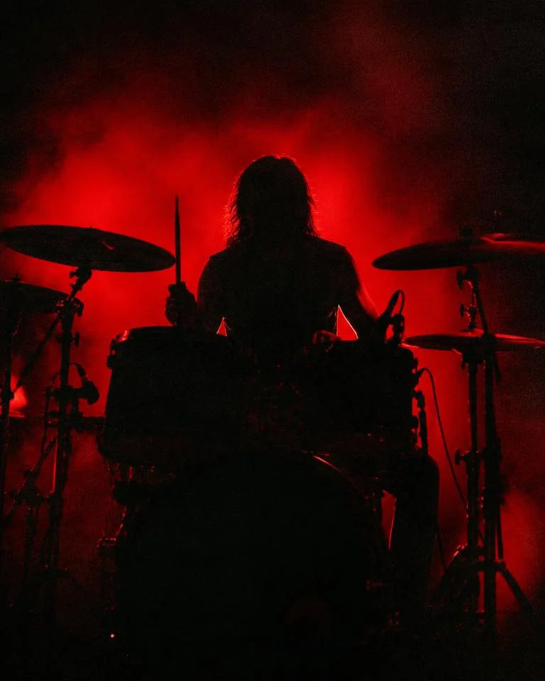 Red-backlit silhouette of a drummer behind the kit
