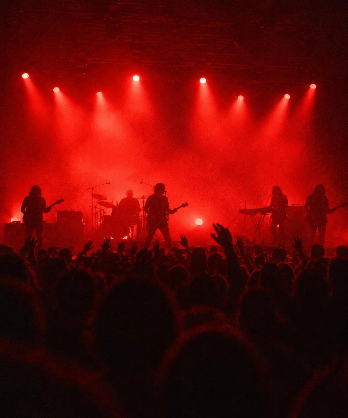 Full band on stage in red light, seen from the crowd