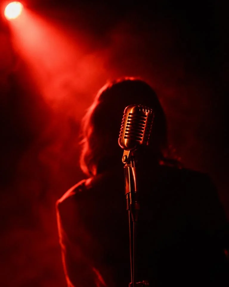 Vintage chrome microphone under a red spotlight with a vocalist silhouette