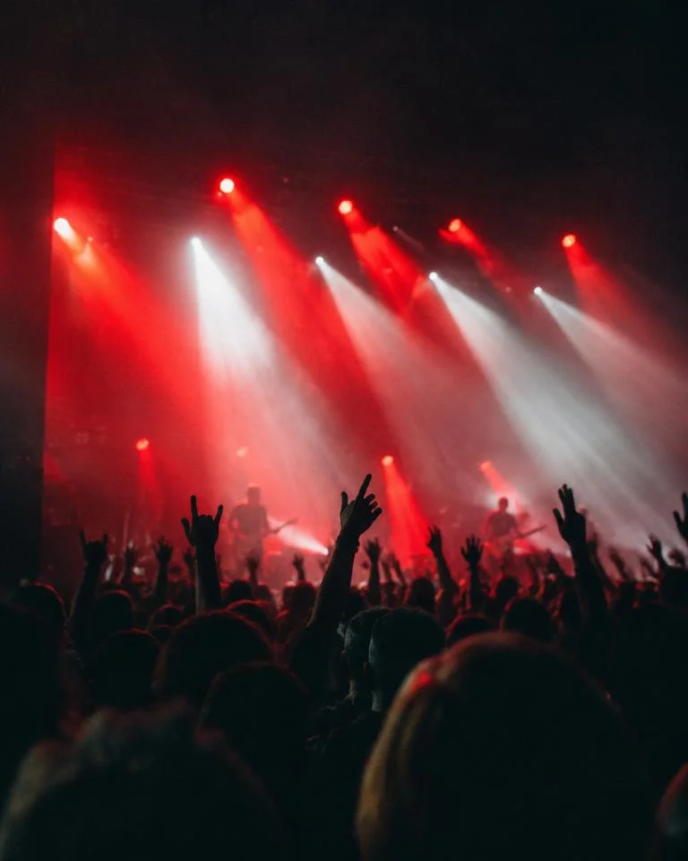Concert crowd with hands raised under red and white stage beams