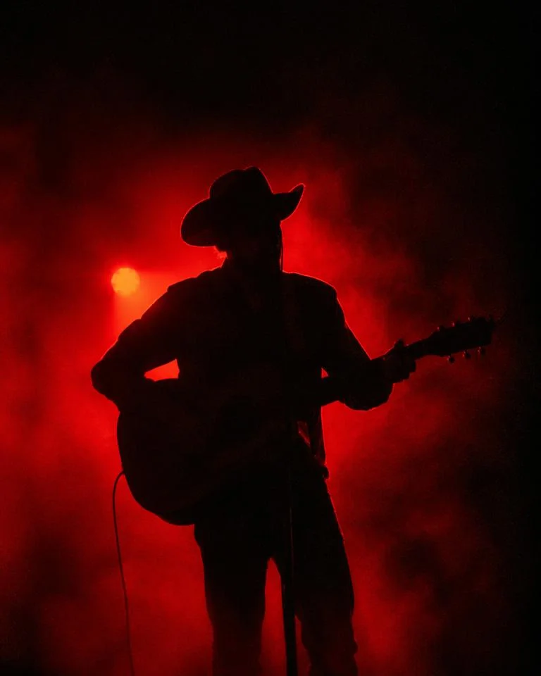 Guitarist in a cowboy hat silhouetted by red backlight